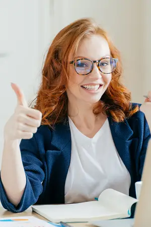 Smiling woman in glasses giving a thumbs up gesture in a workplace setting