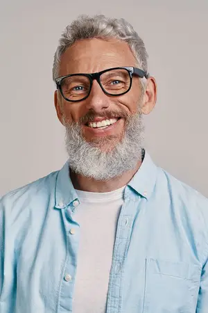 Smiling man with gray hair and beard wearing glasses and a blue shirt with a pocket