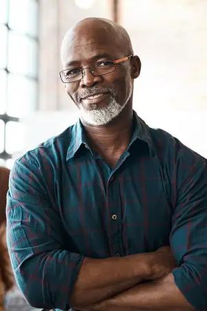 Portrait of a man with glasses standing with his arms crossed in an indoor setting