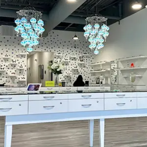 A modern interior design with white shelves, a white table, and blue chandeliers, possibly a shop with a person sitting in the background.