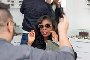 A woman wearing sunglasses is trying them on in a store with a man and other people in the background