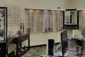 An indoor area with various glasses displayed on the wall, a desk, a computer monitor, and a person in the mirror.