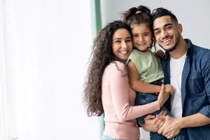 A family of three, a man and woman with a young girl in between them, smiling