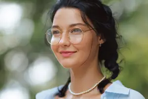 A woman wearing glasses and a pearl necklace is smiling