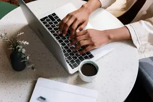 A person sitting on a chair while working on a laptop with a cup of coffee on the table