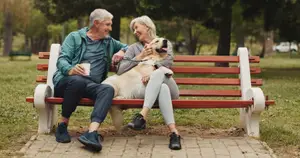 An elderly couple with their dog sitting on a bench in a park during the daytime