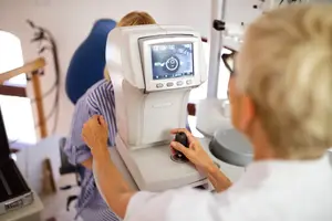 An optometrist is using an eye examination machine to check a patient's vision in a clinic.