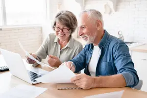 A couple sitting in a kitchen looking at papers and a laptop