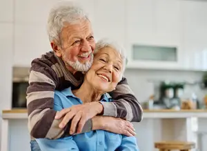 Elderly couple standing in kitchen smiling and hugging each other