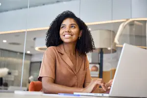 Woman sitting at desk with laptop smiling at the camera