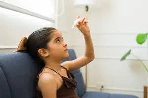 Girl sitting on a couch holding an eyedropper bottle in her hand.