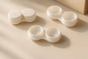 Four white contact lens cases arranged on a beige surface