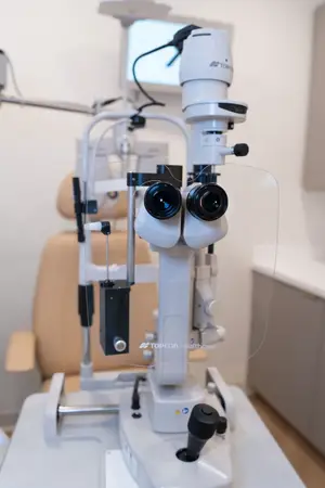 A Topcon Healthcare ophthalmic microscope on a table with a clear plastic shield and a beige chair in the background.