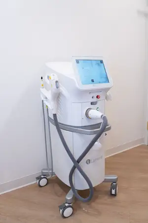 Image of a white laser hair removal machine with a monitor and a gray hose on wheels in a room