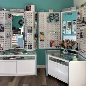 Optical store display with various eyeglasses on white panels, turquoise walls, and a vase of flowers.