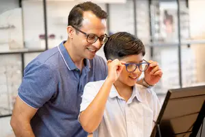 father helping son try on new eyeglasses