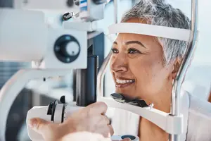 A woman with short gray hair is getting her eyes checked by an optometrist in a clinic.