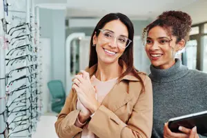 Two women are smiling and looking at glasses in a store.