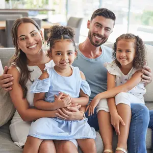 A smiling family of four sitting on a couch, with two girls and their parents.