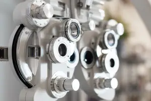 An optometrist's equipment, including a phoropter, is shown up close, with adjustable lenses and dials visible.