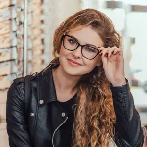 A smiling woman with curly hair wearing black glasses and a black leather jacket.
