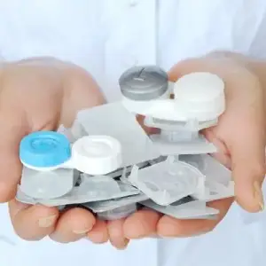 A person in a white shirt holds multiple transparent plastic containers for lenses, likely in a medical setting.