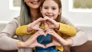 A woman and a girl are making a heart shape with their hands while smiling and posing for a photo