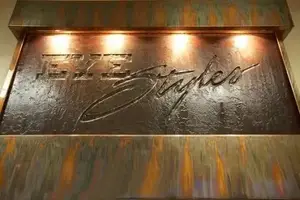 Bronze metal plaque with the word Eye Staples in a fancy font with a copper tint