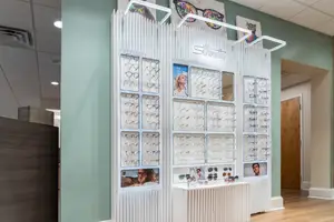 An optical shop with a white display case full of glasses, and a wall with a green color and a wooden door at the right side.