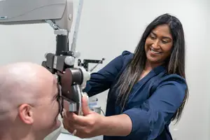 A woman optometrist is examining a male patient's eyes with a device in a clinic.