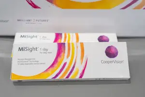 Two boxes of MiSight 1 day contact lenses are displayed on a gray surface, with colorful designs on the boxes and a purple circle on the front of each box. The boxes are arranged in a row, and a white box with the text 'Brilliant Futures' is behind them.