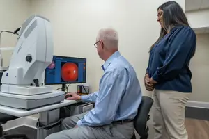A man is looking at a computer screen with a woman standing behind him in an office room.