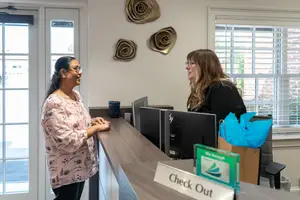 Two women are smiling and talking to each other in front of a reception desk