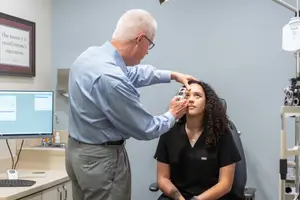 A male doctor is examining a female patient's eyes in an examination room.