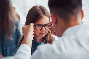 A young girl is having her glasses adjusted by a man who is probably her father, in an office.