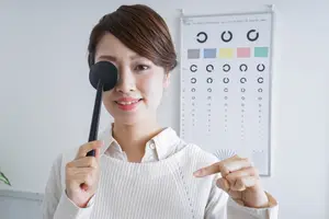 Woman in white sweater holding an eye chart and smiling