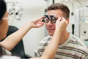 A person wearing glasses is adjusting a man's eye glasses in a medical setting