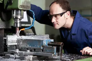 A man is operating a machine in a factory while wearing protective eyewear.