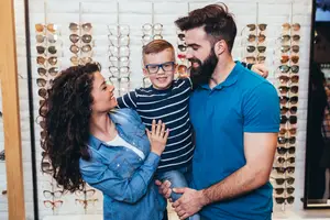 A man, woman, and young boy are standing in front of a display of sunglasses in a store.