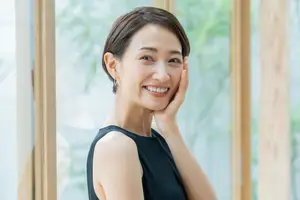 An East Asian woman with short hair is smiling and posing for a photo while standing in front of a glass wall.