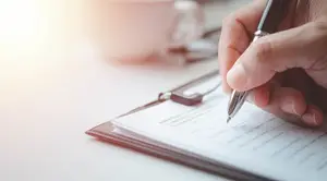 A person filling out a form on a clipboard with a pen.