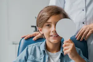 A boy holding a white paper circle in front of his eye while a doctor is adjusting his head.