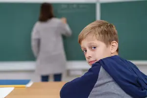 A boy looks at a woman writing on a chalkboard in a classroom