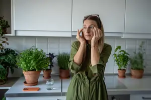 A woman in a green dress is standing in a kitchen and looking upward with her hands on her face.
