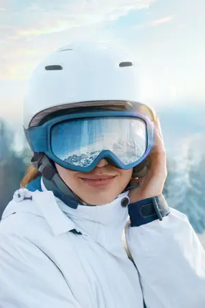 A woman is smiling while adjusting her white helmet and goggles on a snowy mountain.