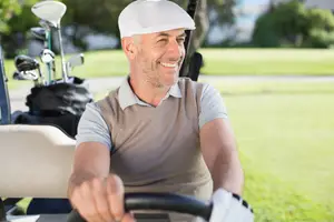 A man drives a golf cart and smiles for the camera at a golf course.
