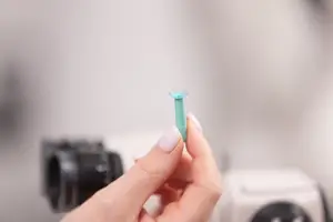 A hand holding a small blue object with a microscope in the background