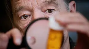 An older man is examining a bottle of medicine with a magnifying glass