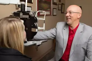 A man in a suit is adjusting a machine and smiling at a woman in front of him in an office.