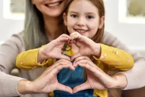A woman and a young girl are smiling and making a heart shape with their hands